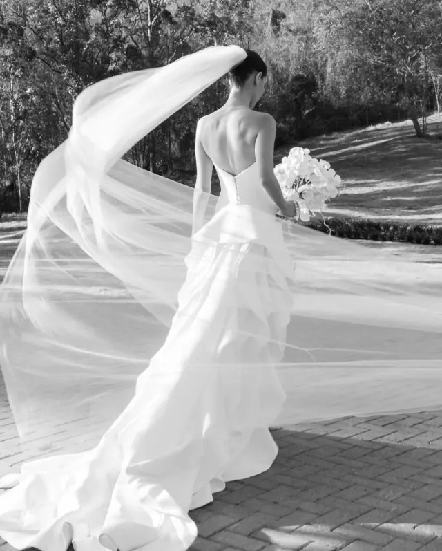 Noiva vista de costas em um vestido branco, com o véu ao vento em um jardim