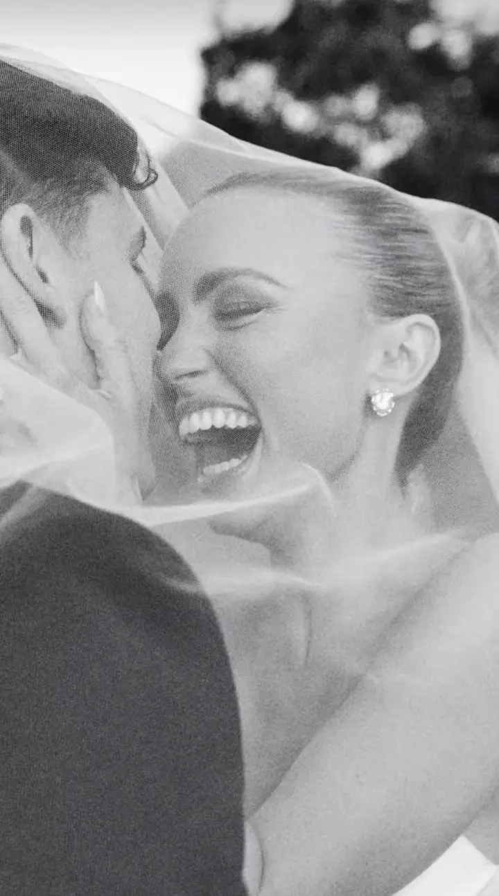 Casal sob o véu, com a noiva sorrindo em uma fotografia em preto e branco.