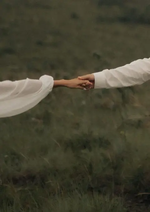 Mãos de um casal entrelaçadas em um campo ao ar livre